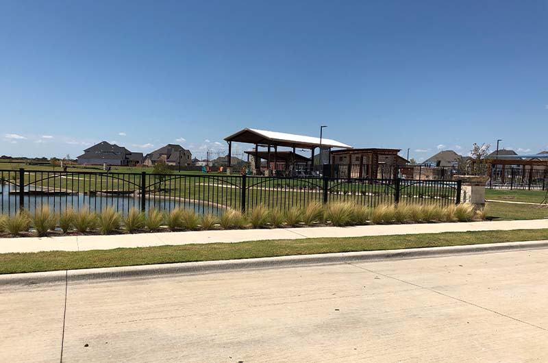 Grassy community center with pond and metal fence