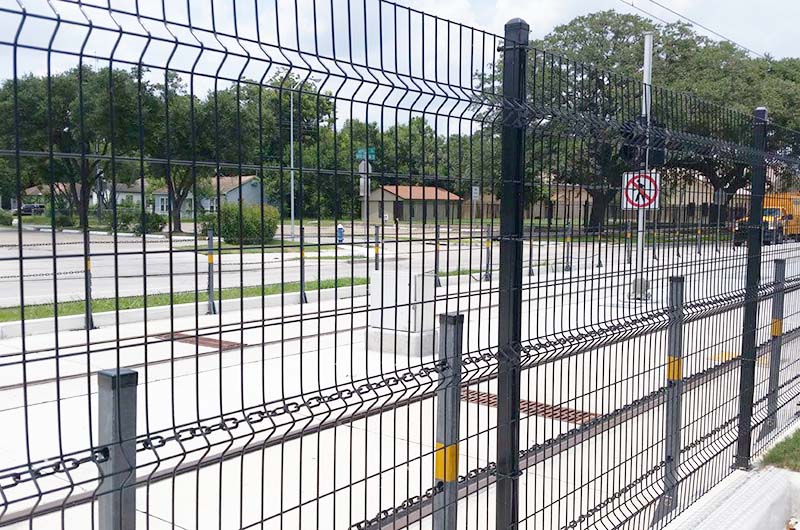 Black metal high-security fence with a ribbed mesh that’s held on with ties to the posts. There is a second, short fence just on the other side that has three chains that run through metal posts.